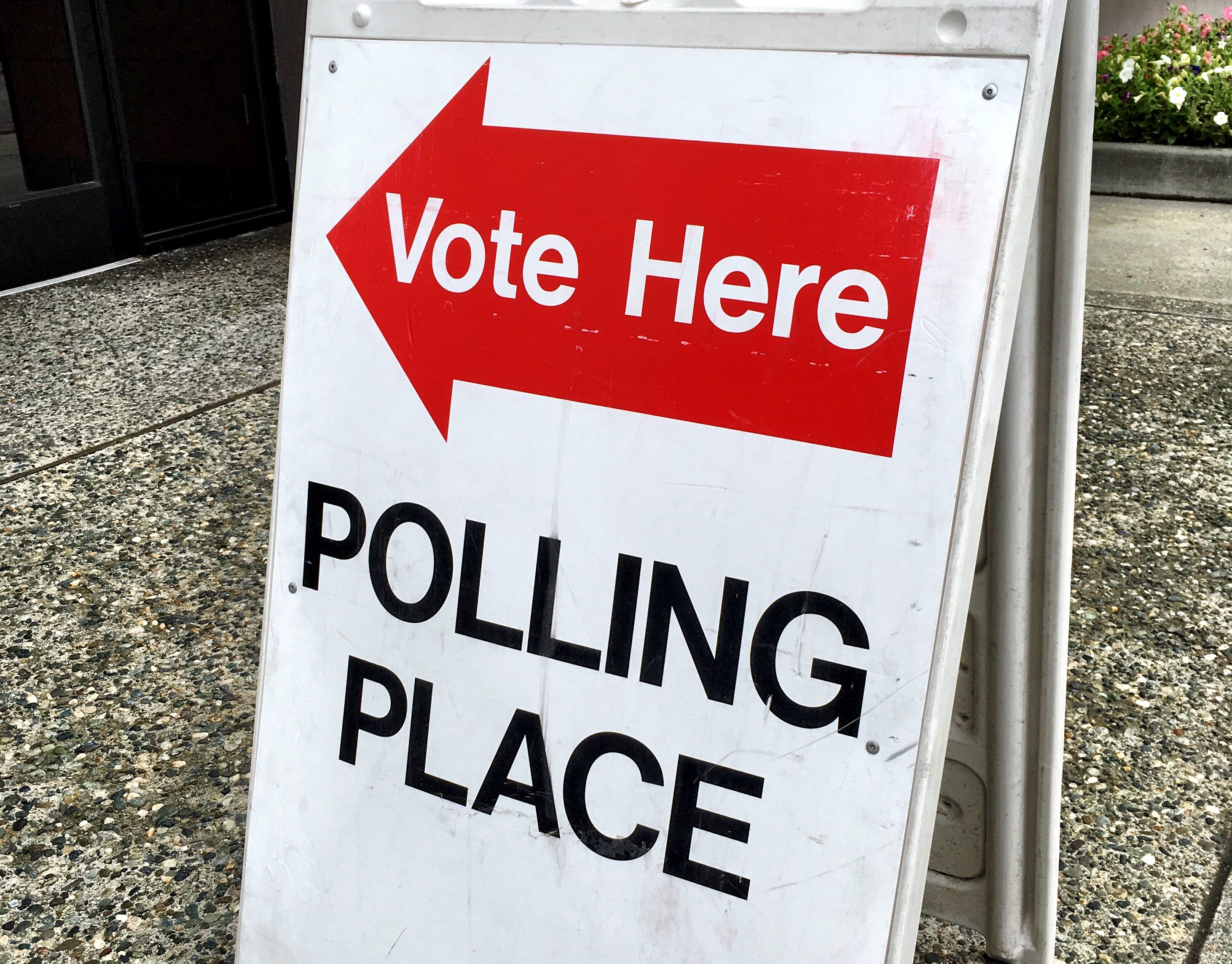 A red arrow with the text 'vote here' and black letters saying 'polling place' are posted on a white fold out sign.