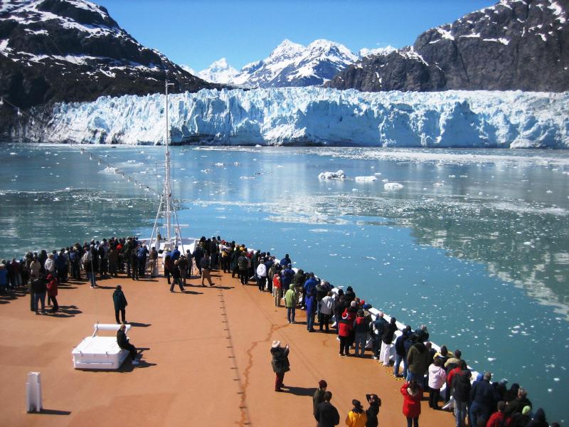 people stand on the dock of a large boat as it approaches a glacier