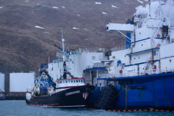 A largeboat tied up to a larger boat near a mountain