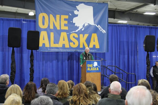 A man speaks in front of a blue banner