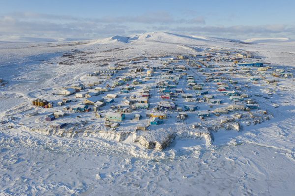 An aerial view of Toksook Bay, showing snow-covered houses in a compact village with snowy sea ice in the foreground.