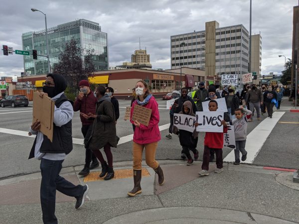 A line of people walk up the street on the sidewalk holding signs