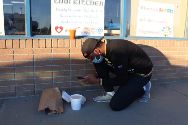 A man in a baseball cap takes a picture of his food on the sidewalk