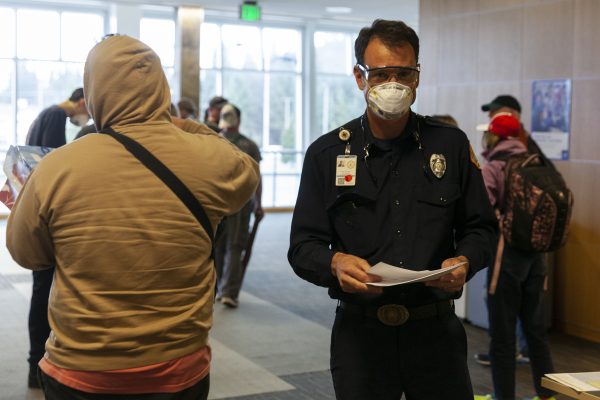 A man in a police uniform and a facemassk talks to passengers 