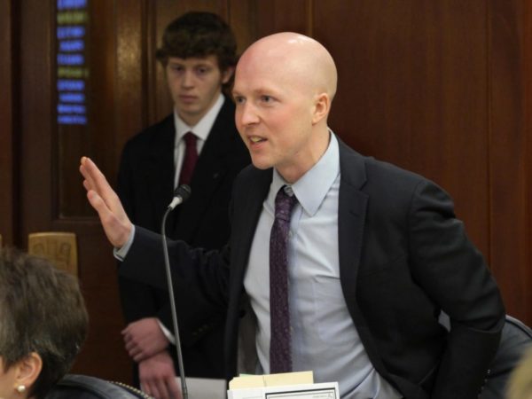 A white man with a bald head speaks into a microphone