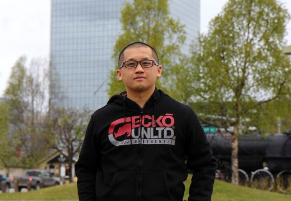 A man in a hoody andd a glasses and short hair stands looking at the camera