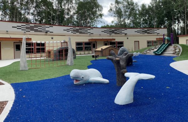 An outdoor playground features climbing equipment unique to Alaska Native culture, including a gillnet, sod house and beluga.