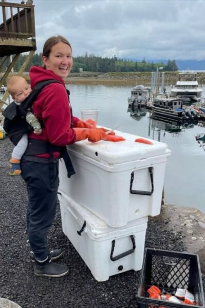 a woman with a baby cutting salmon on a cooler